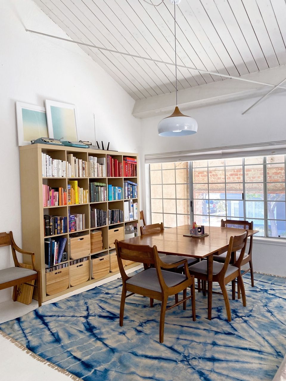 Mid-century modern dining space with wood shelving, geometric rug, and shiplap ceiling