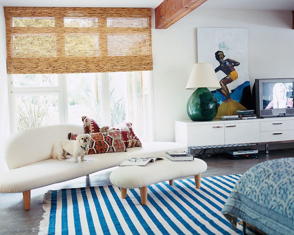 Bright mid-century modern living room with coastal vibes, striped blue rug, cream sofa, and natural wood accents