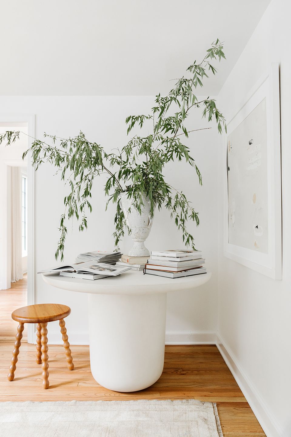 Minimalist white space with cascading green plant and natural wood stool, serene aesthetic