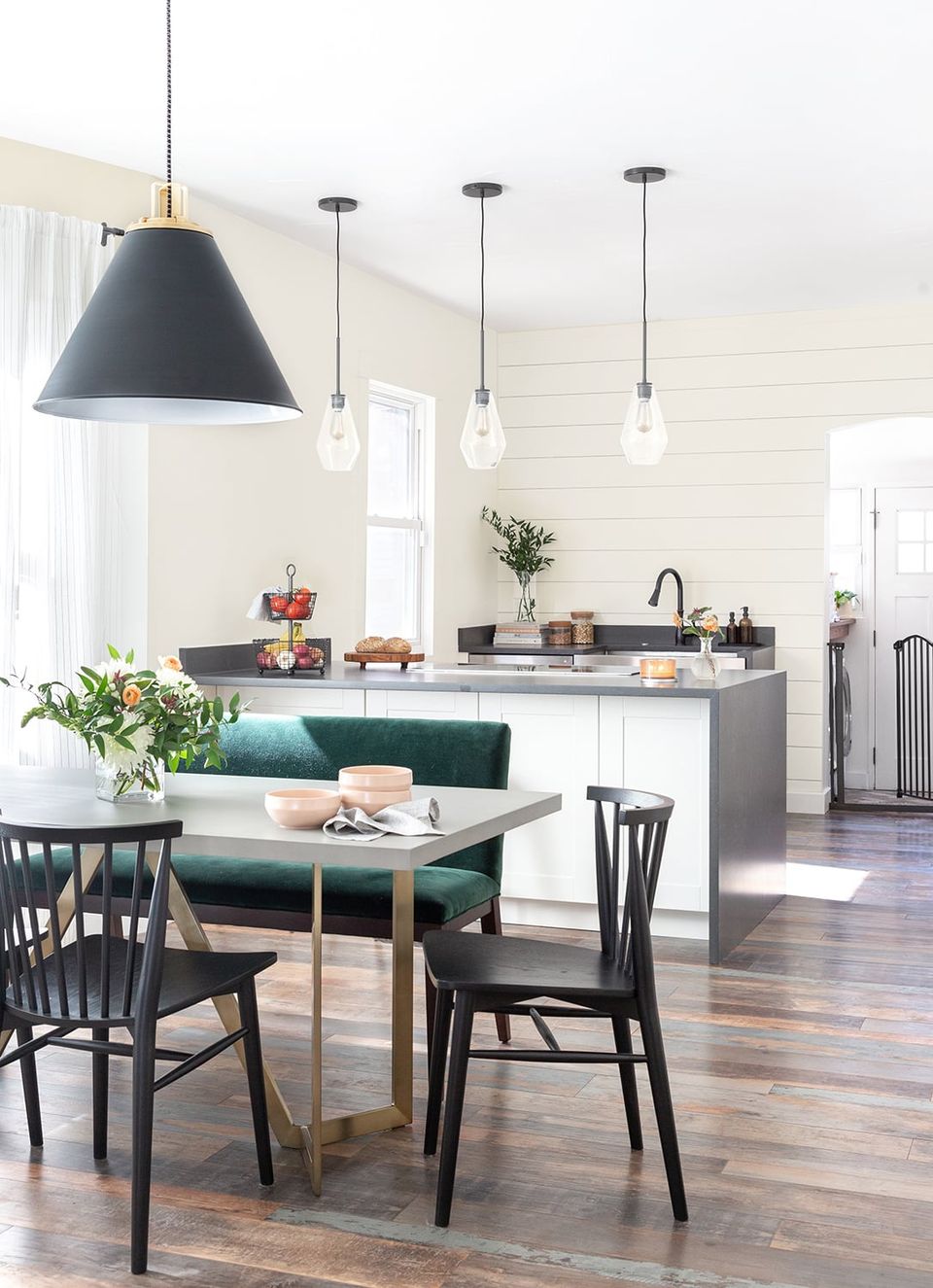 Modern farmhouse kitchen-dining blend: warm white shiplap, black pendant lights, emerald green banquette