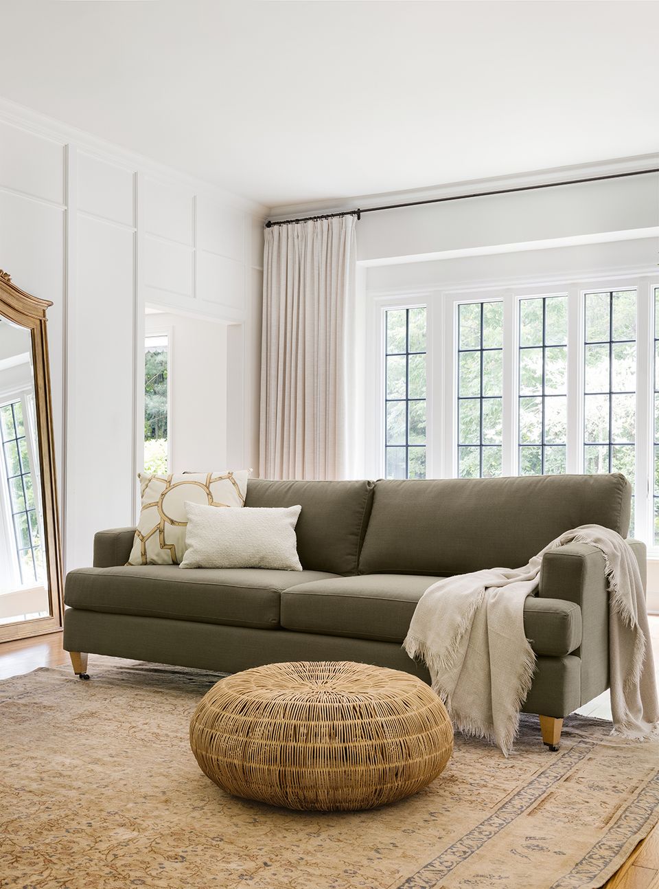 Neutral living room with sage green sofa, woven ottoman, and cream accents creating a calm, organic aesthetic.