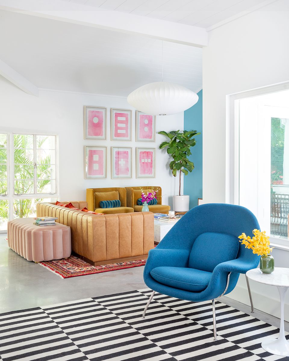 Eclectic modern living space with bold color blocking: mustard sofa, cobalt chair, pink gallery wall, and geometric rug