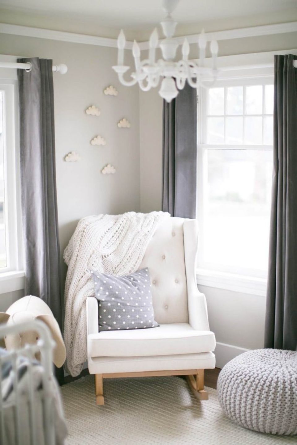 Serene neutral nursery featuring elegant chandelier, gray accents, white glider chair, and soft cloud wall decals.