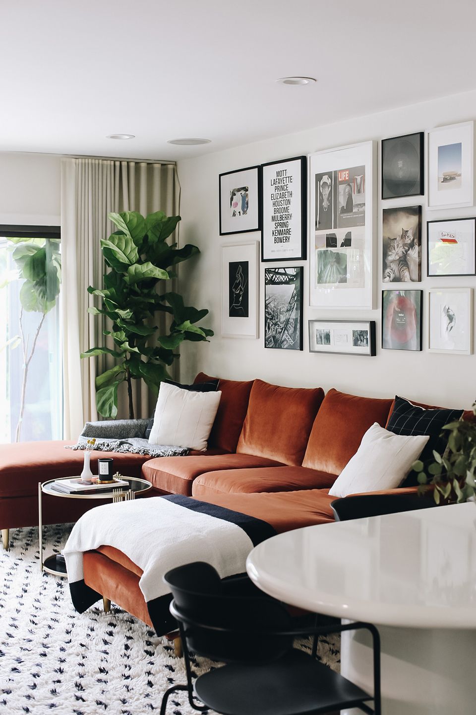 Contemporary living room featuring rust leather sofa, gallery wall art, and greenery in monochromatic palette