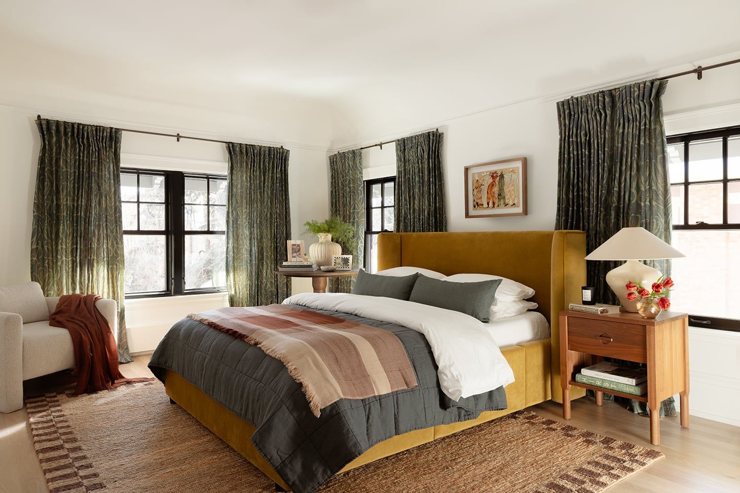 Warm bedroom with mustard headboard, sage green curtains, striped bedding, and natural wood accents