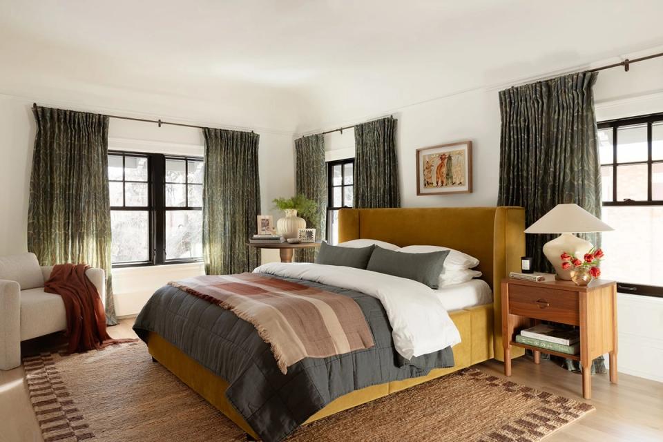 Warm bedroom with mustard headboard, sage green curtains, striped bedding, and natural wood accents