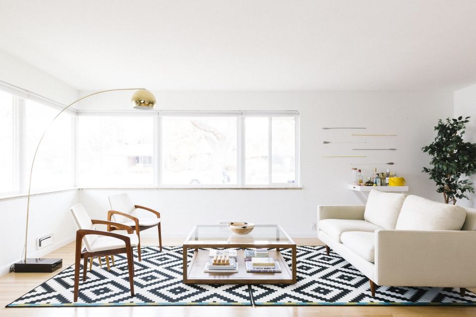 Bright mid-century modern living room with warm wood chairs, geometric rug, and minimalist aesthetic