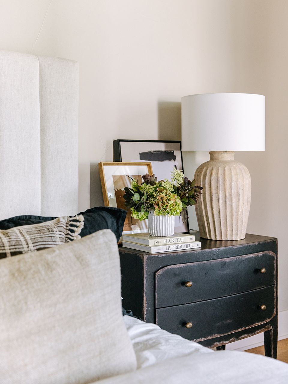 Minimalist nightstand styling with black dresser, ceramic lamp, greenery, and neutral textiles