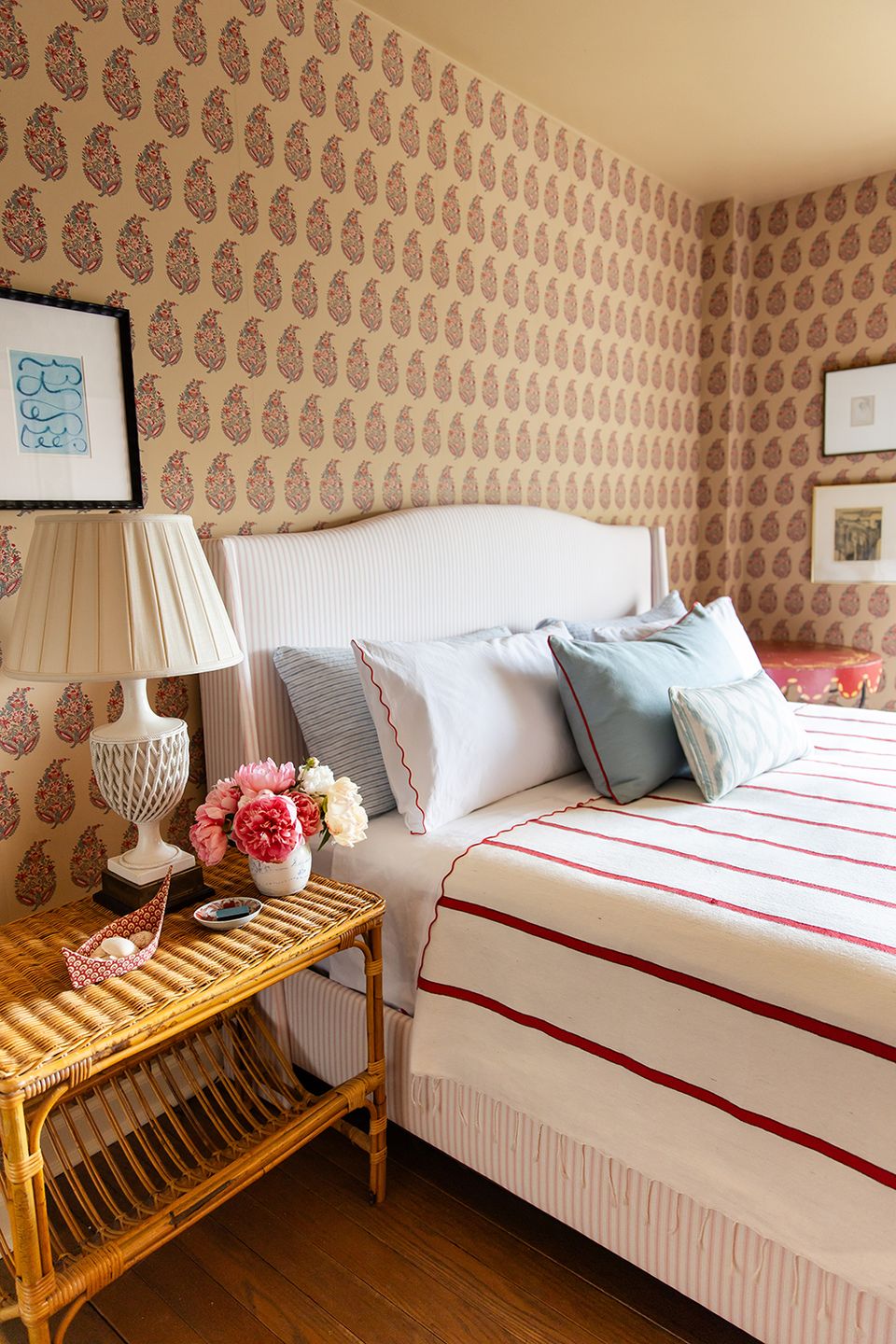 Cozy maximalist bedroom with patterned wallpaper, striped bedding, and rattan nightstand in warm tones