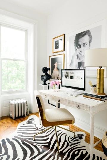 Minimalist home office in pristine white with brass accents, monochrome zebra rug, and curated gallery wall styling.