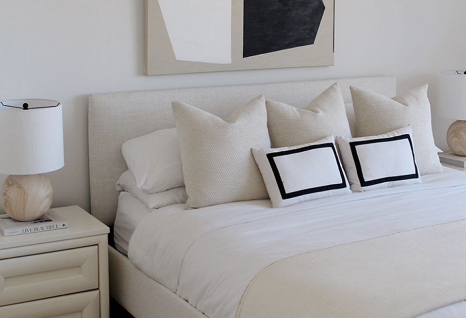 Serene minimalist bedroom with cream bedding, neutral pillows, and modern abstract artwork