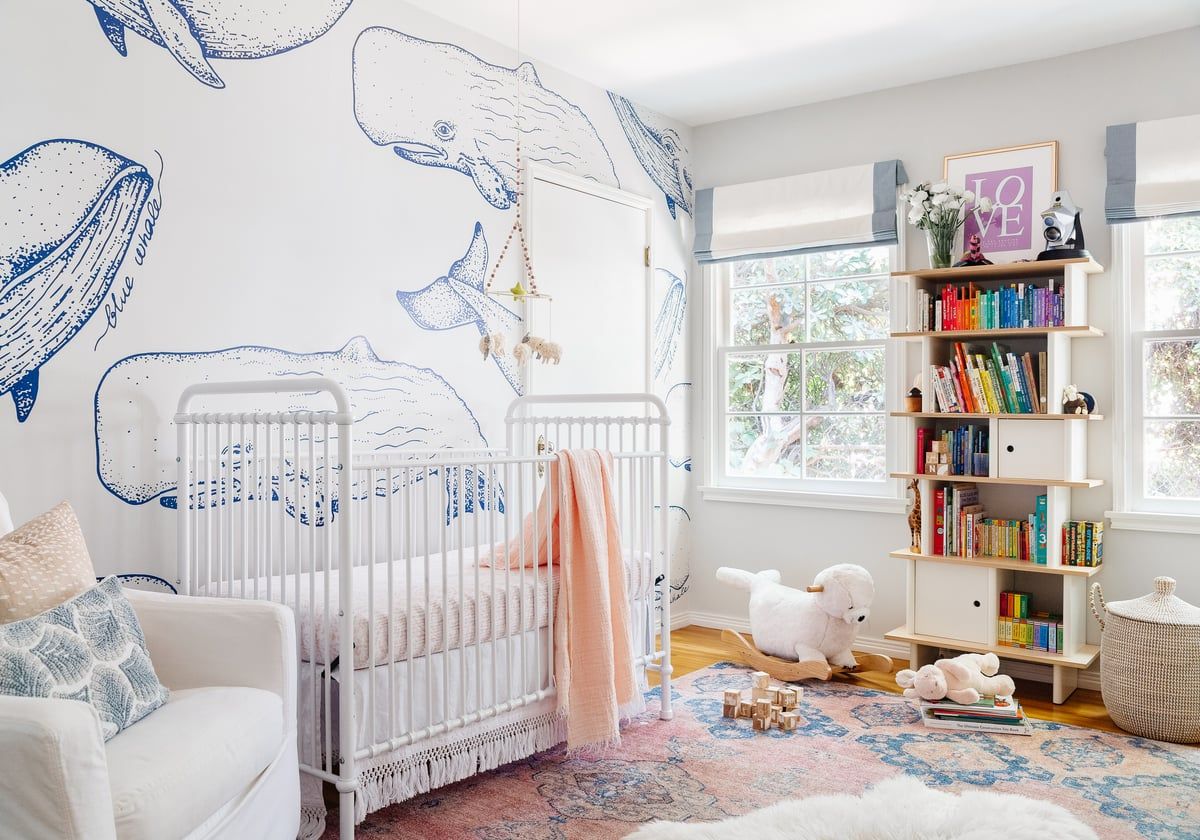 Serene coastal nursery with whale murals, white crib, blush accents, and pastel watercolor rug creating a soft, whimsical atmosphere