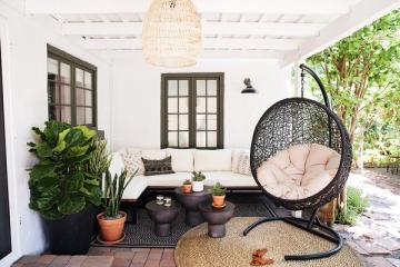 Modern bohemian covered patio with clean lines, neutral palette, woven egg chair, and lush foliage