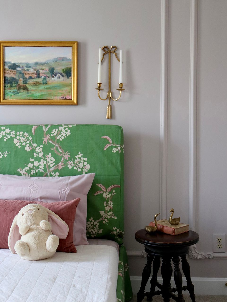 Eclectic bedroom with emerald green floral headboard, brass sconces, and vintage landscape art