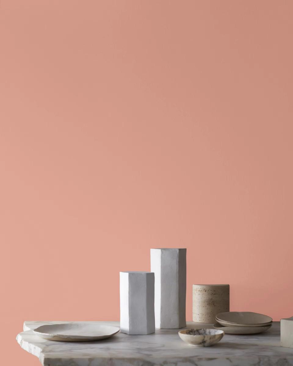 Modern minimalist setup on marble surface against dusty rose wall with neutral ceramic vessels and metallic accents