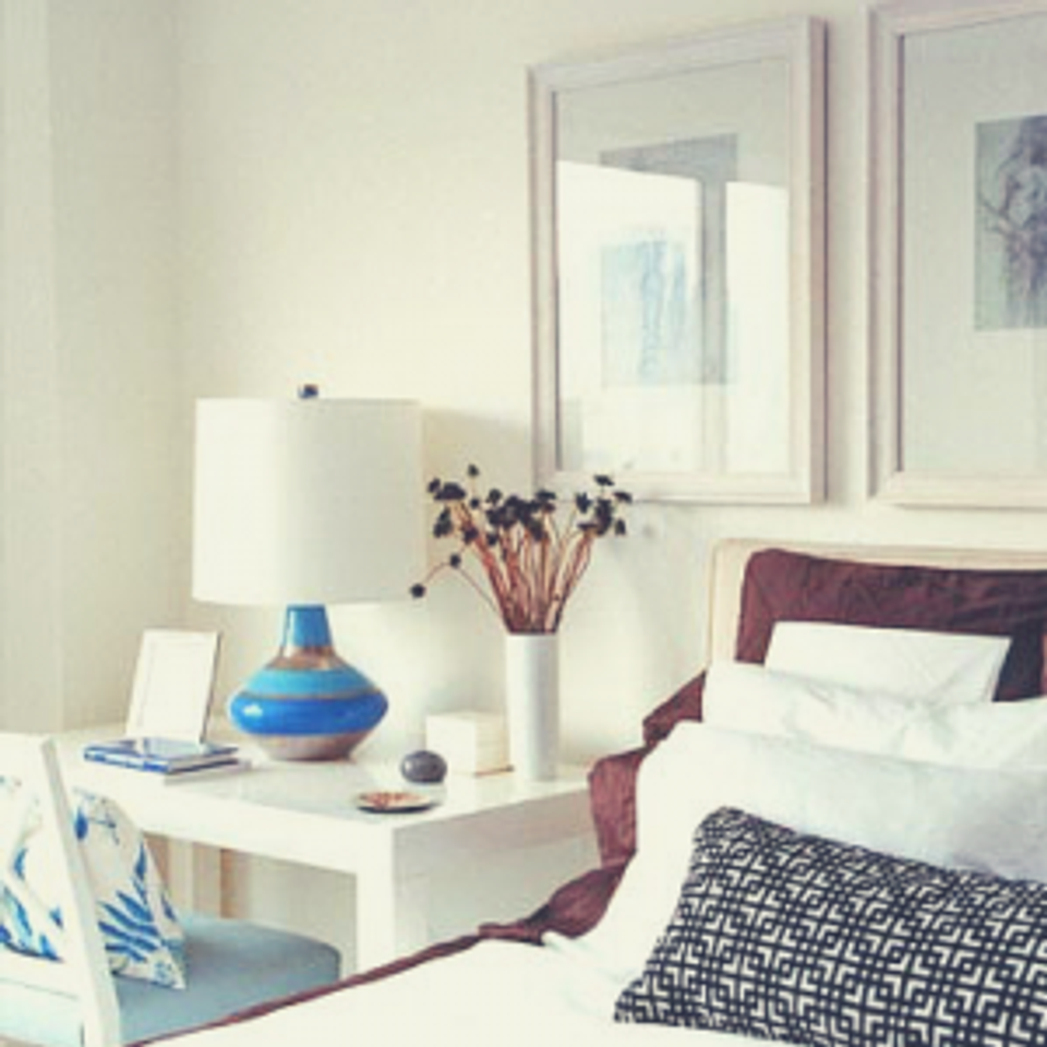 Bedroom nightstand styling with white Parsons desk, sapphire lamp, and jewel-tone bedding contrast