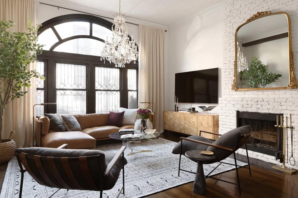 Transitional living room blending warm cognac leather, cream drapery, exposed brick, and an arched window for timeless elegance