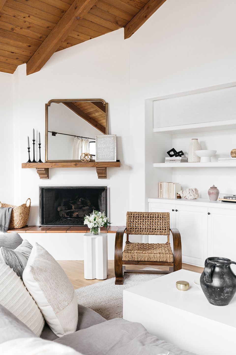 Scandinavian fireplace nook with natural wood beams, woven chair, and neutral palette