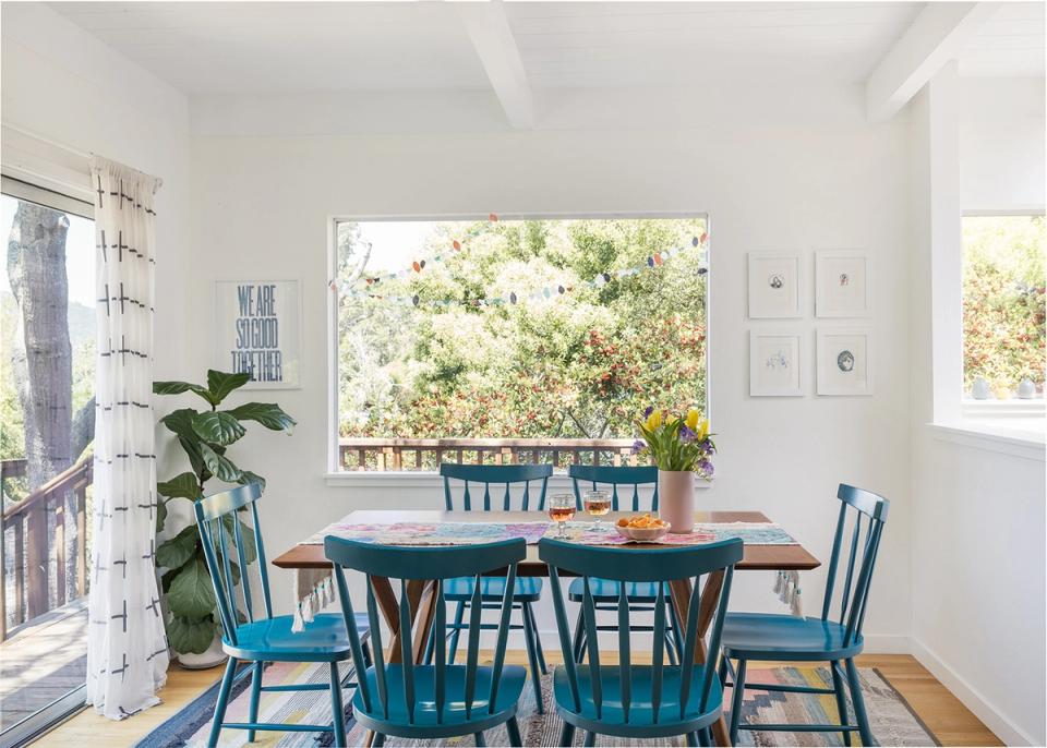Bright coastal dining room with navy chairs, teal table, natural light, and lush greenery creating a fresh, inviting gathering space
