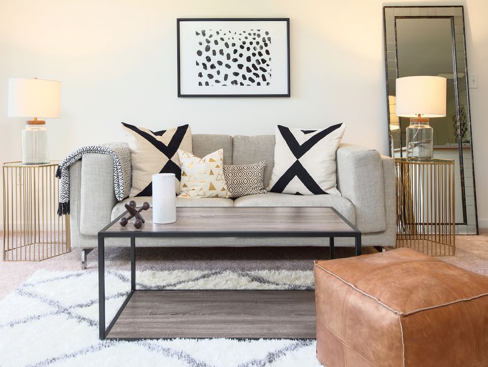 Neutral transitional living room with gray sofa, cognac leather ottoman, black industrial coffee table, and monochrome geometric art.