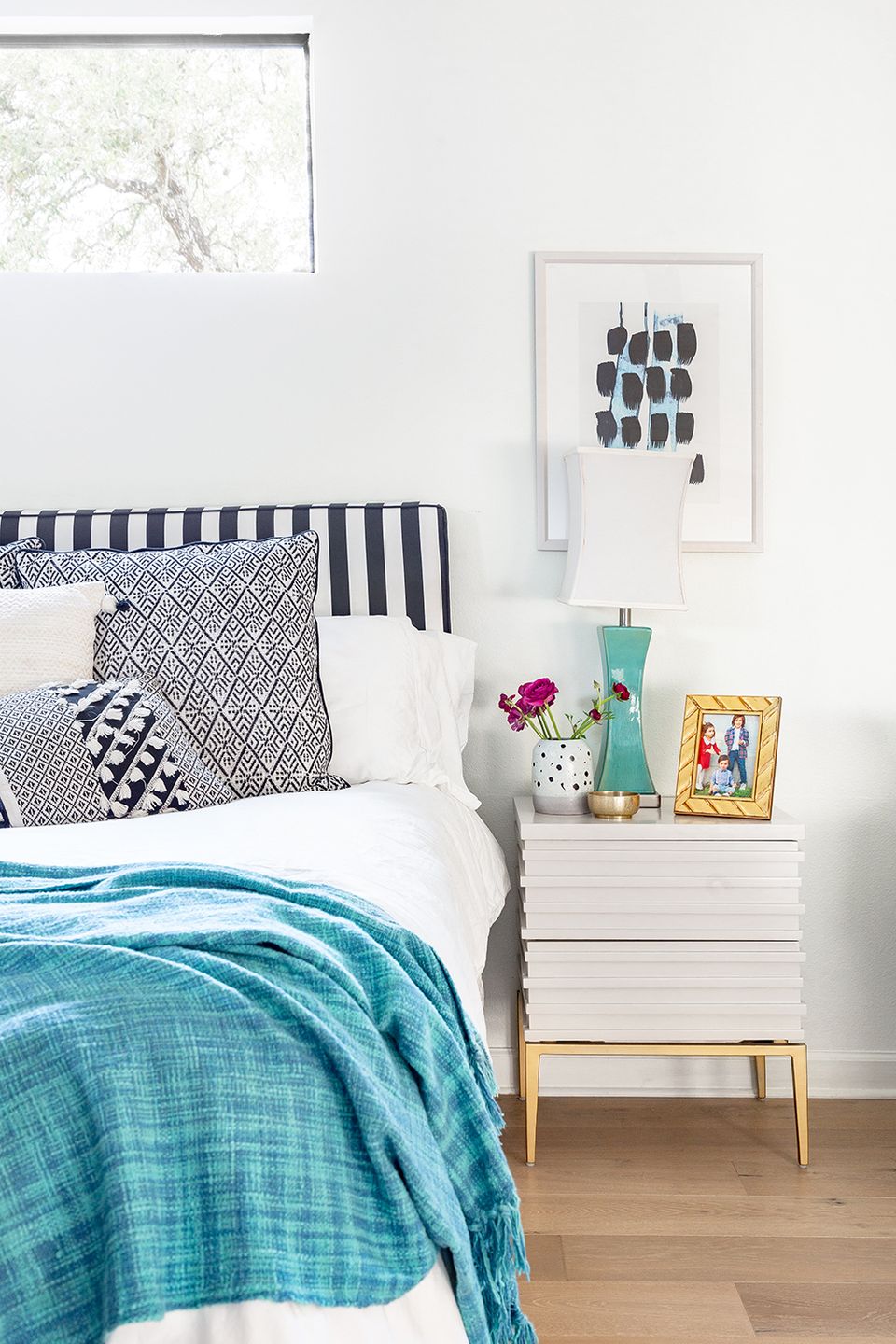 Eclectic preppy bedroom blending navy and white geometric patterns, turquoise textured throw, white nightstand, and playful modern art accents