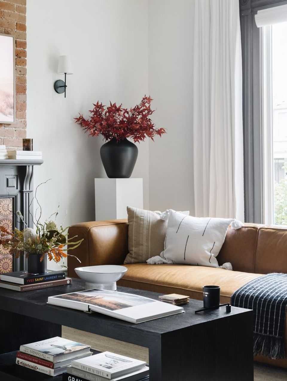 Modern industrial living room with cognac leather sofa, dramatic burgundy floral arrangement, and black coffee table