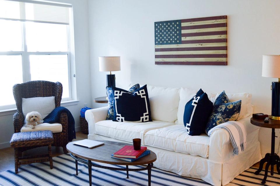 Preppy living room with cream sofa, navy accents, striped rug, and vintage flag art