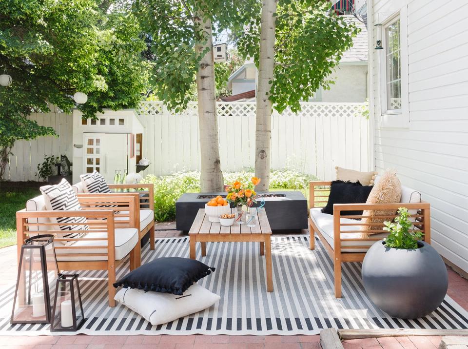 Modern backyard oasis with striped outdoor rug, natural wood furniture, and contemporary black accents