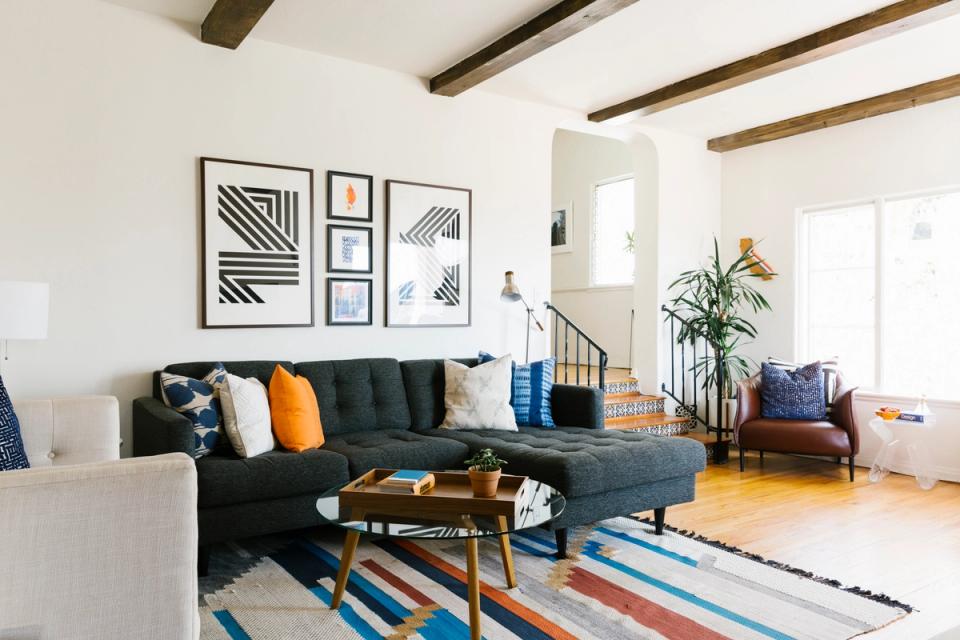 Modern masculine living room with dark sectional, warm wood beams, geometric wall art, and colorful striped area rug