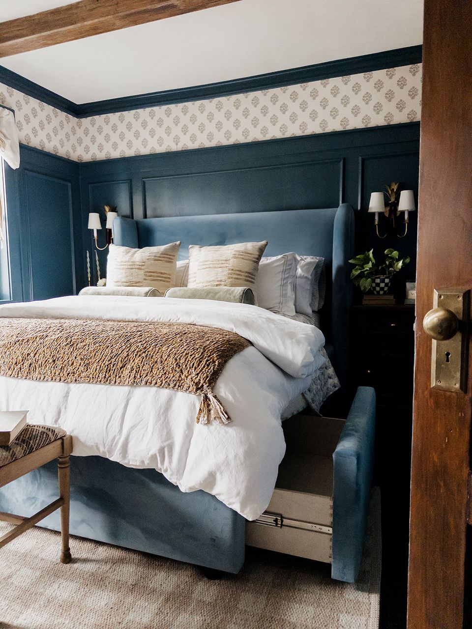 Traditional bedroom: navy blue upholstered bed, gold accents, patterned wallpaper, warm wood details