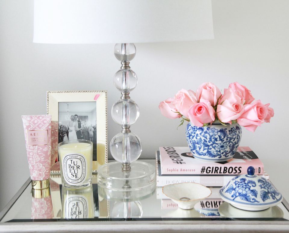 Chic feminine vanity styling with pink roses, crystal candlestick, and blue porcelain accents on neutral backdrop