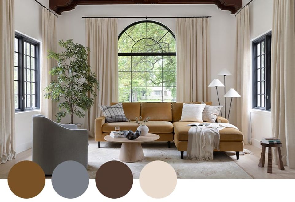 Transitional living room blending warm ochre, gray, and cream tones with arched windows, caramel leather sectional, and lush greenery.