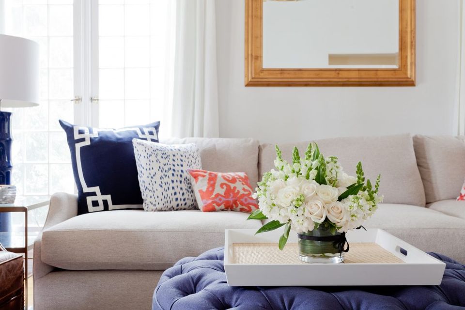 Transitional living room with neutral sofa, navy accents, coral florals, and natural light creating a fresh, welcoming mood.