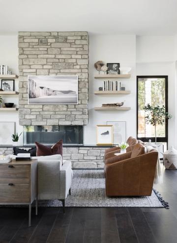 Contemporary living room with light brick fireplace, neutral palette, brown leather chair, and curated gallery wall creating warm, inviting atmosphere