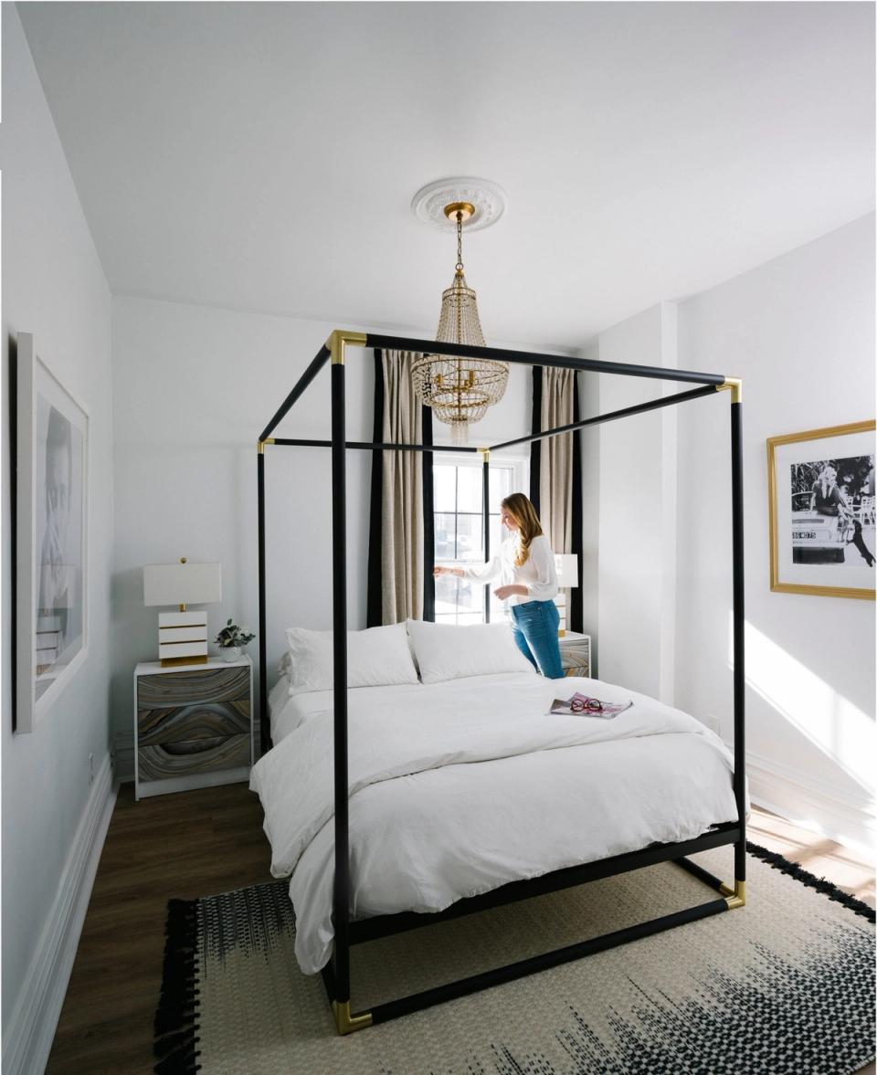 Bright minimalist bedroom with black four-poster bed, white linens, and brass accents creating a modern, airy aesthetic