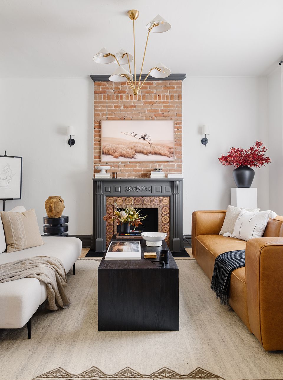 Sophisticated bedroom-living hybrid featuring vintage brick fireplace, cognac leather chair, and elegant brass sculptural sconce