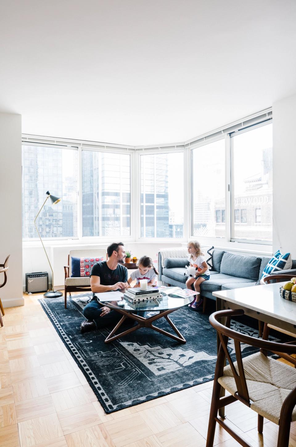 Contemporary open-plan homeschool with floor-to-ceiling windows, mid-century furniture, and navy area rug.