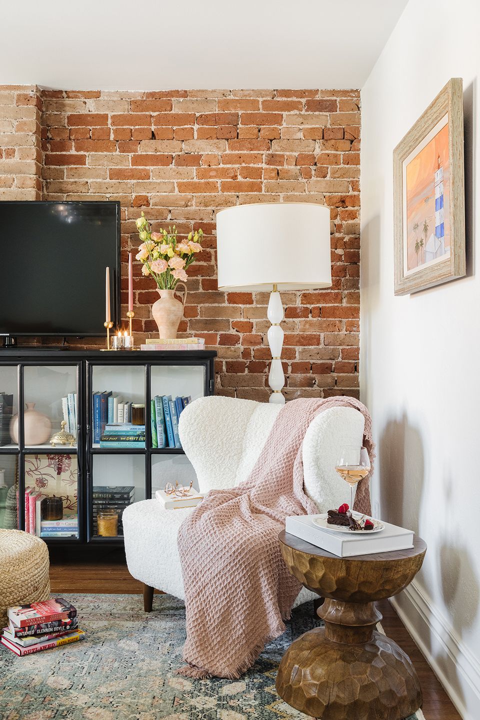 Cozy reading chair with exposed brick backdrop, warm lighting, brass accents, and soft pink throw in eclectic space.