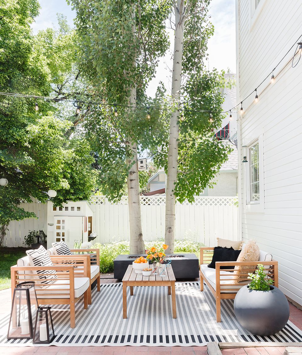 Contemporary Scandinavian patio with striped rug, wooden furniture, and dappled tree shade