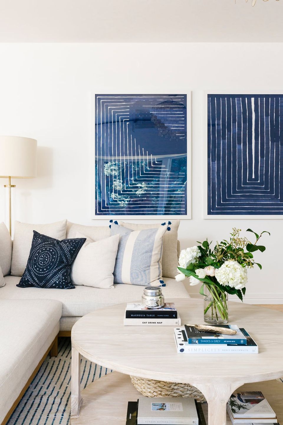 Coastal-inspired living room with navy geometric wall art, cream sofa, and blue accent pillows against white walls