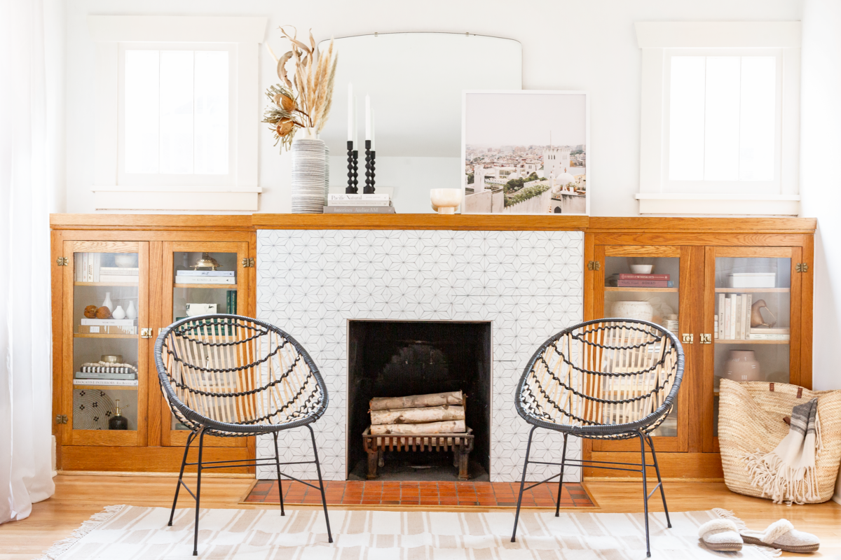 Mid-century modern fireplace nook with warm wood cabinetry, geometric woven chairs, and painted white subway tile surround