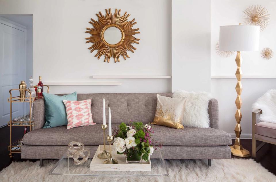 Modern minimalist living room with gray sofa, sunburst mirror, and soft pink and gold accents