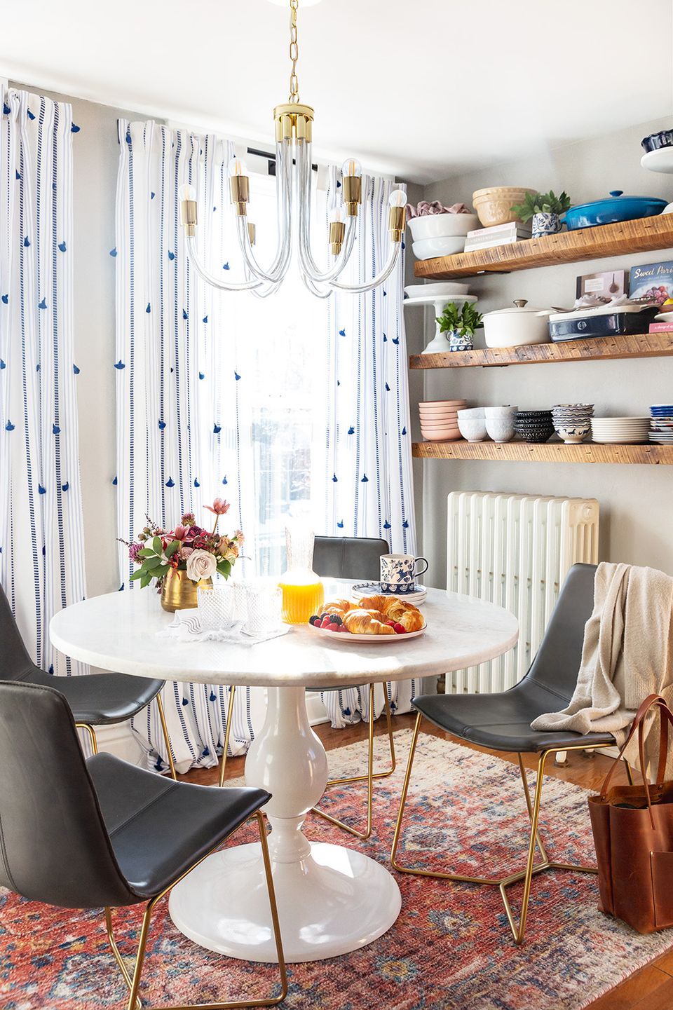Bright breakfast nook with white polka-dot curtains, brass chandelier, colorful rug, and contemporary round white table