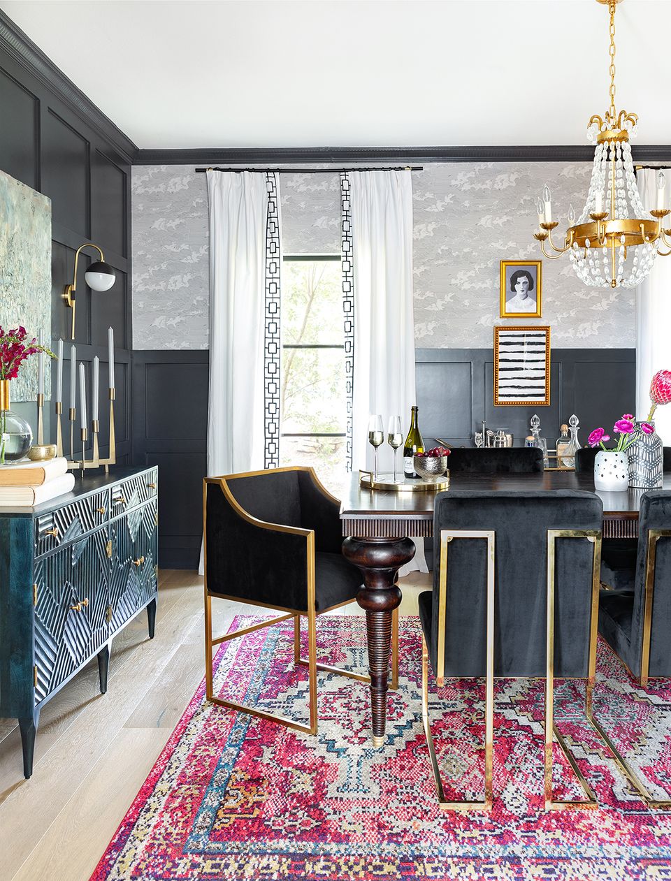 Eclectic maximalist dining room blending dark navy walls, gold fixtures, vibrant pink patterned rug, and bold geometric textiles