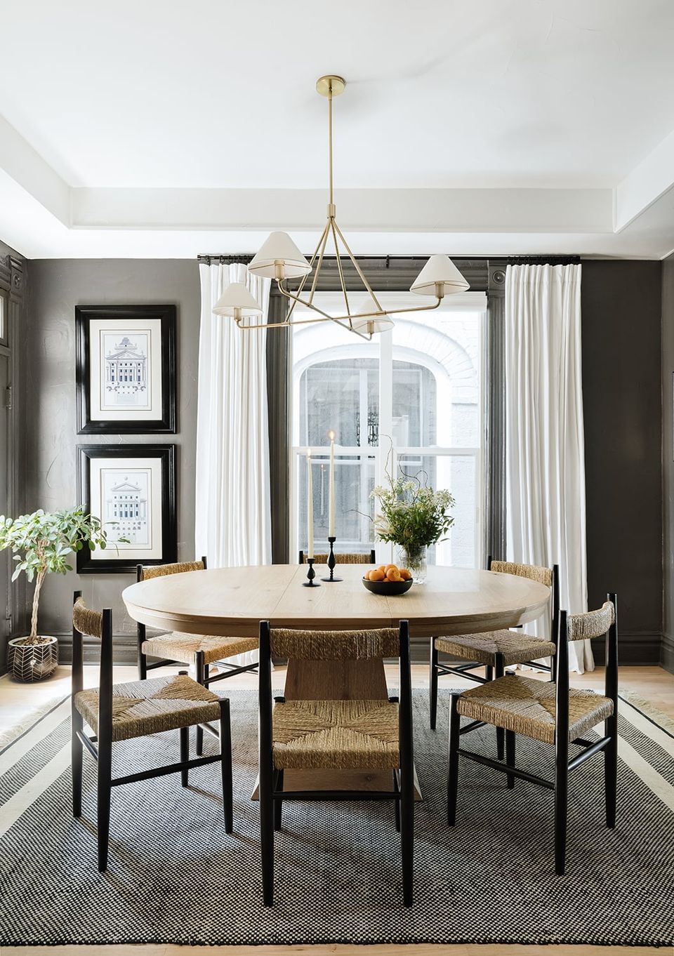 Sophisticated dining room with charcoal walls, round wood table, woven chairs, and brass pendant light
