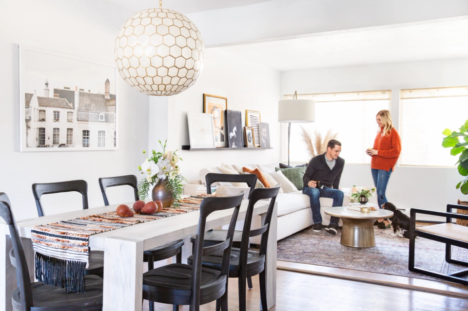 Bright Parisian farmhouse dining area with white table, black chairs, and golden pendant light fixture