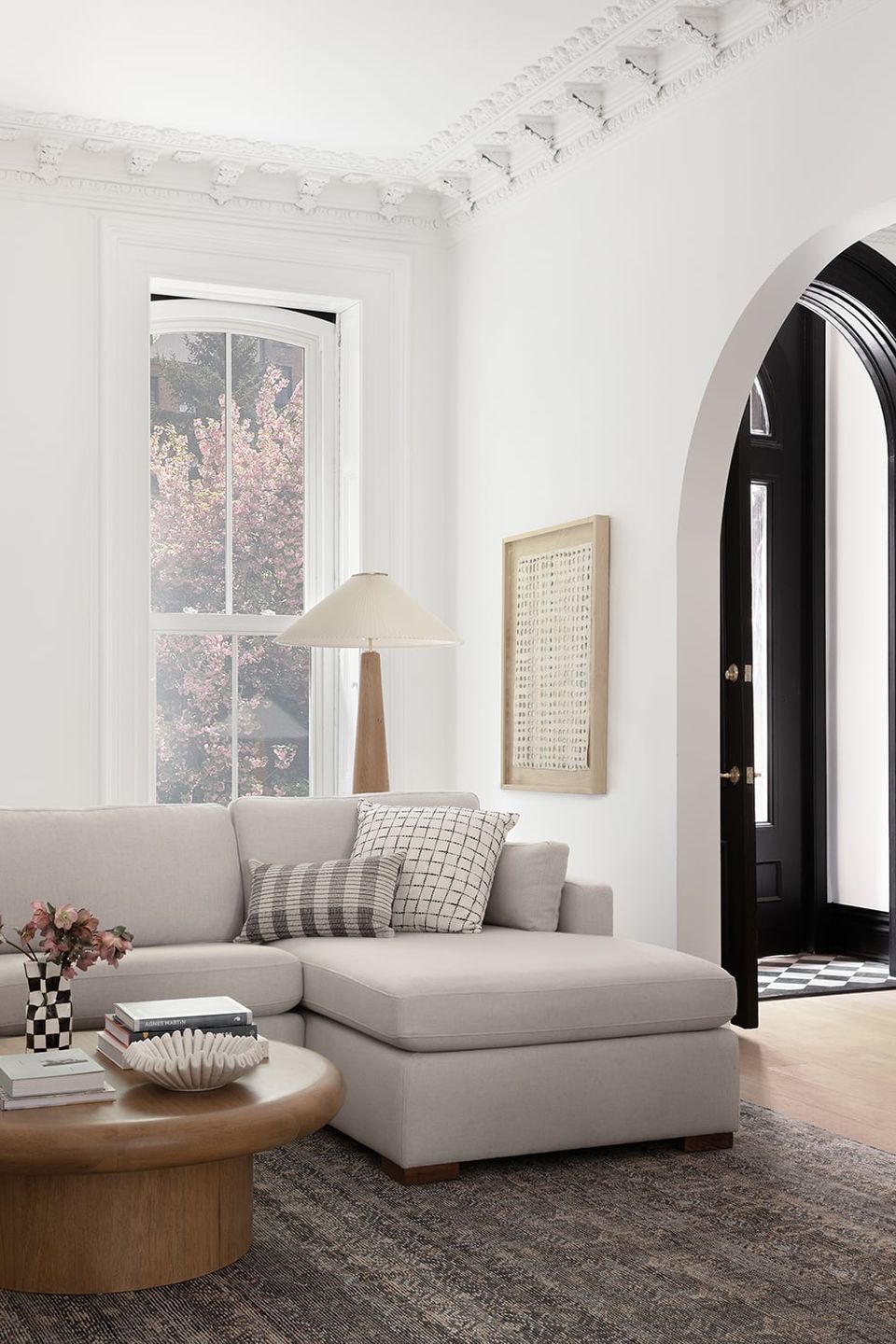 Minimalist Victorian room with cream sectional, black arched door, and soft natural light
