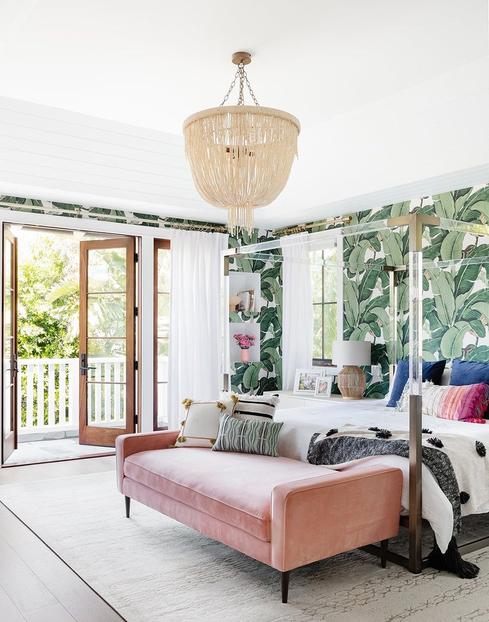 Tropical-inspired bedroom with bold botanical wallpaper, coral velvet bench, and natural beaded chandelier