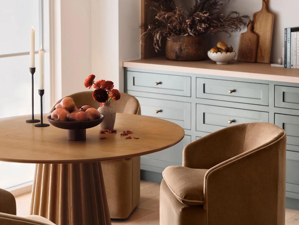 Minimalist dining space with round wooden table, soft furnishings, and seafoam storage creating warm, inviting atmosphere