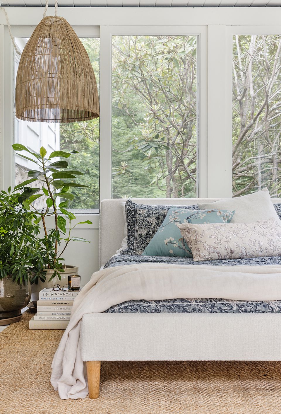 Serene bedroom with natural light, woven pendant lamp, potted plants, and soft neutral bedding in earthy botanical style